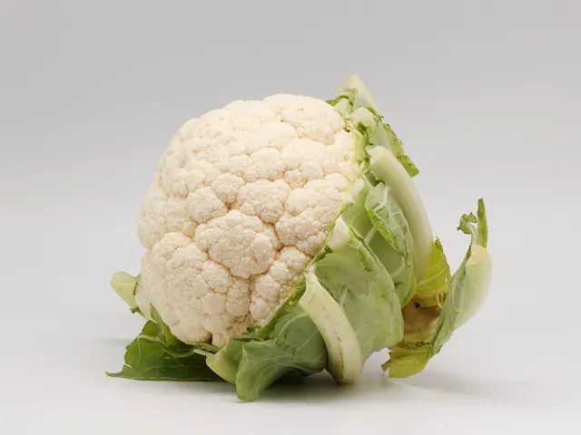 A white cauliflower head with its green leaves.